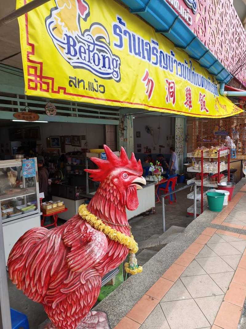 รูปปั้นไก่สีแดงใต้ป้ายร้านสีเหลือง